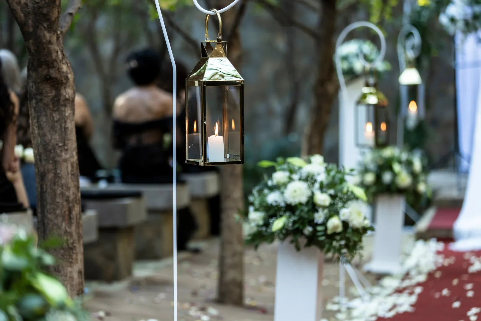 Garden ceremony aisle with white floral pedestals and hanging candle lanterns at Usambara Venue