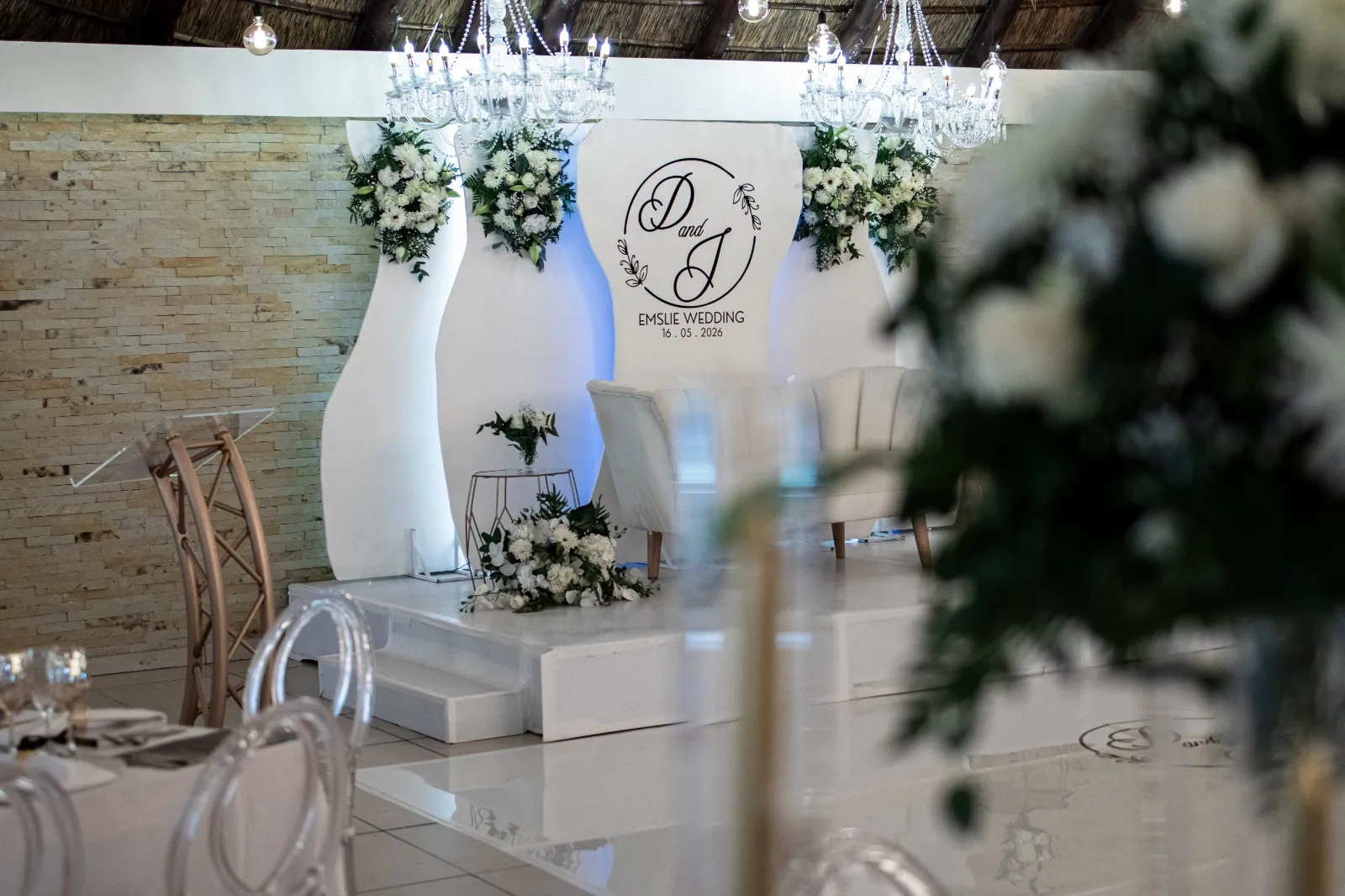 Monogrammed wedding backdrop with white florals and crystal chandeliers on the stage at Usambara Venue