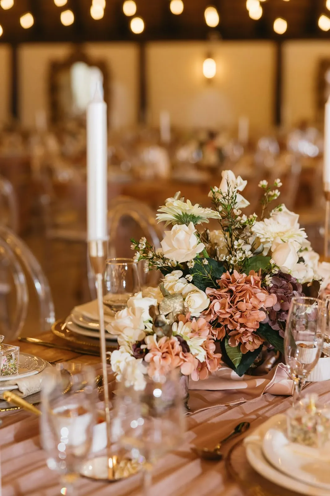 Blush and white flower arrangement beside a taper candle on a reception table at Usambara Venue