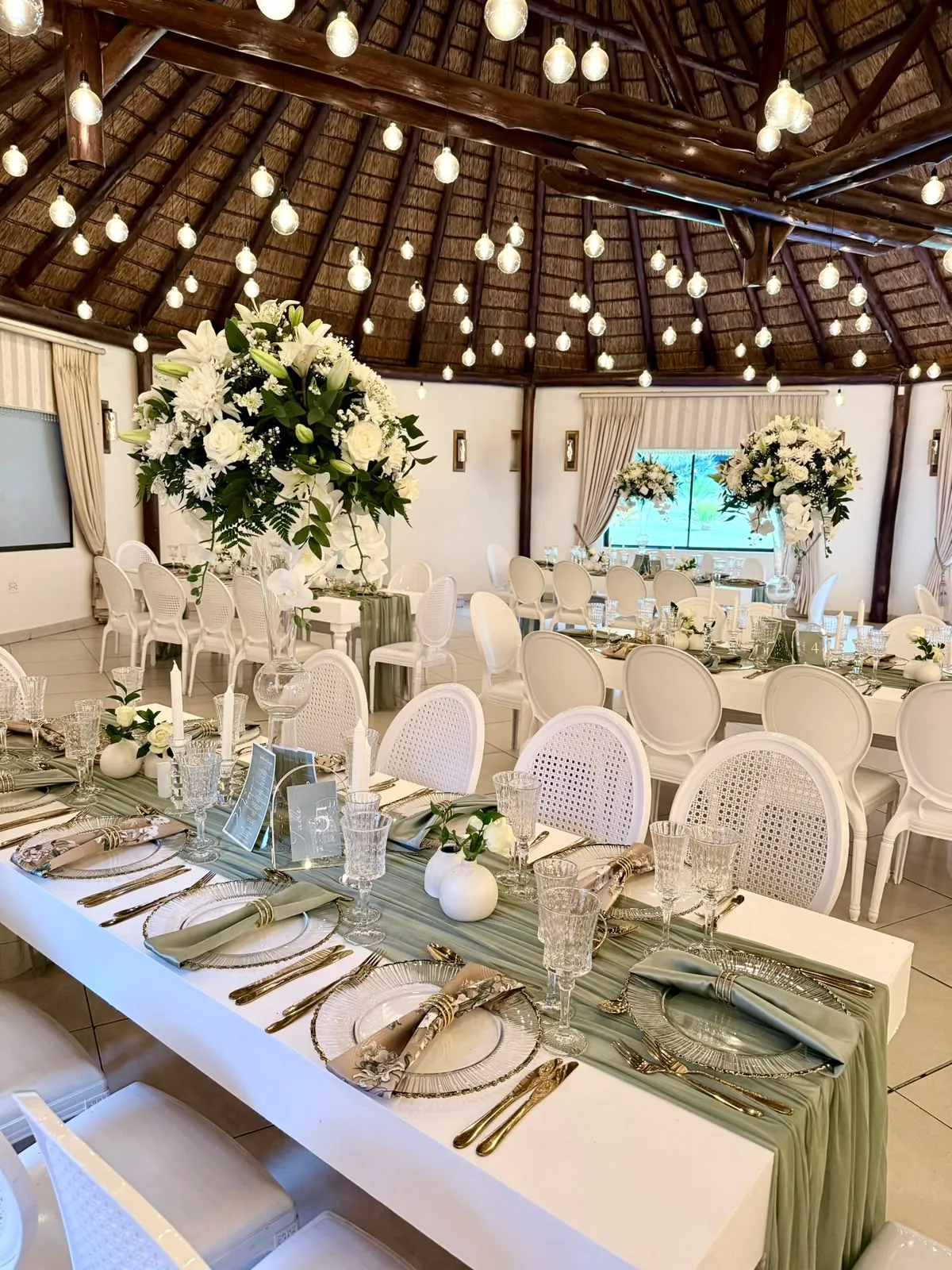 Long table with a sage green runner, white chairs and white floral centrepieces at Usambara Venue